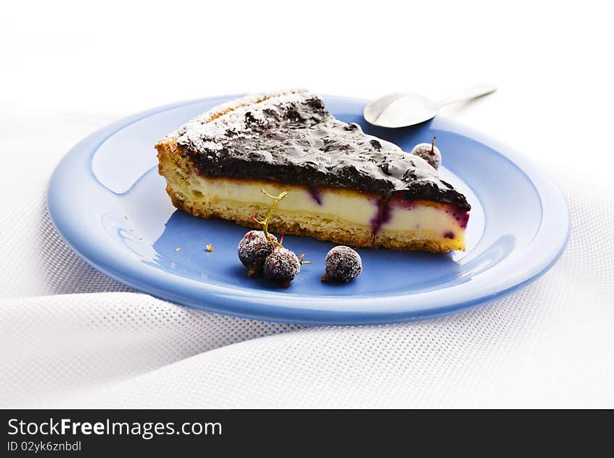 A slice of Blueberries Tart with Black Currant served on a blue platter and on linen tablecloths. A slice of Blueberries Tart with Black Currant served on a blue platter and on linen tablecloths