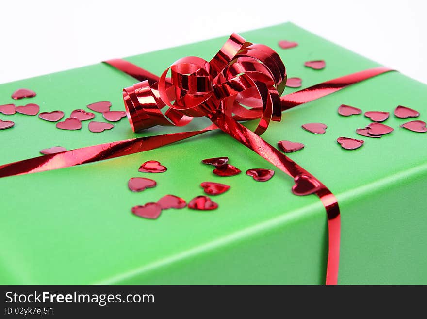 Gift in green wrapping with a red bow decorated with heart shaped confetti in close up. Gift in green wrapping with a red bow decorated with heart shaped confetti in close up