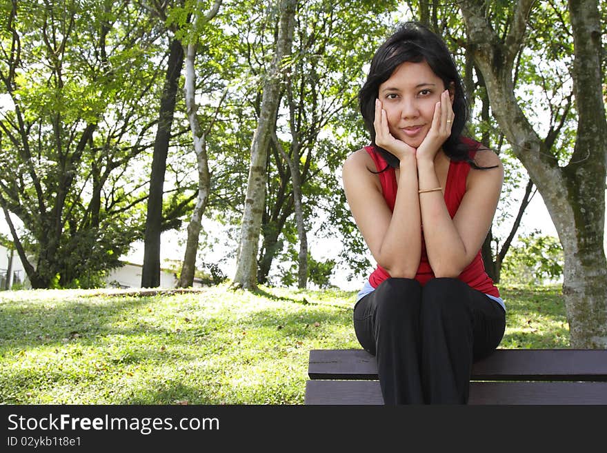 An Asian woman sitting on a bench at a park. An Asian woman sitting on a bench at a park