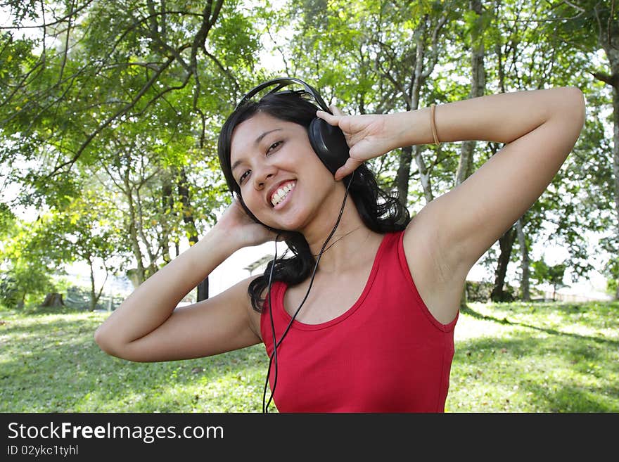 An Asian woman listening to music on headphones at a park