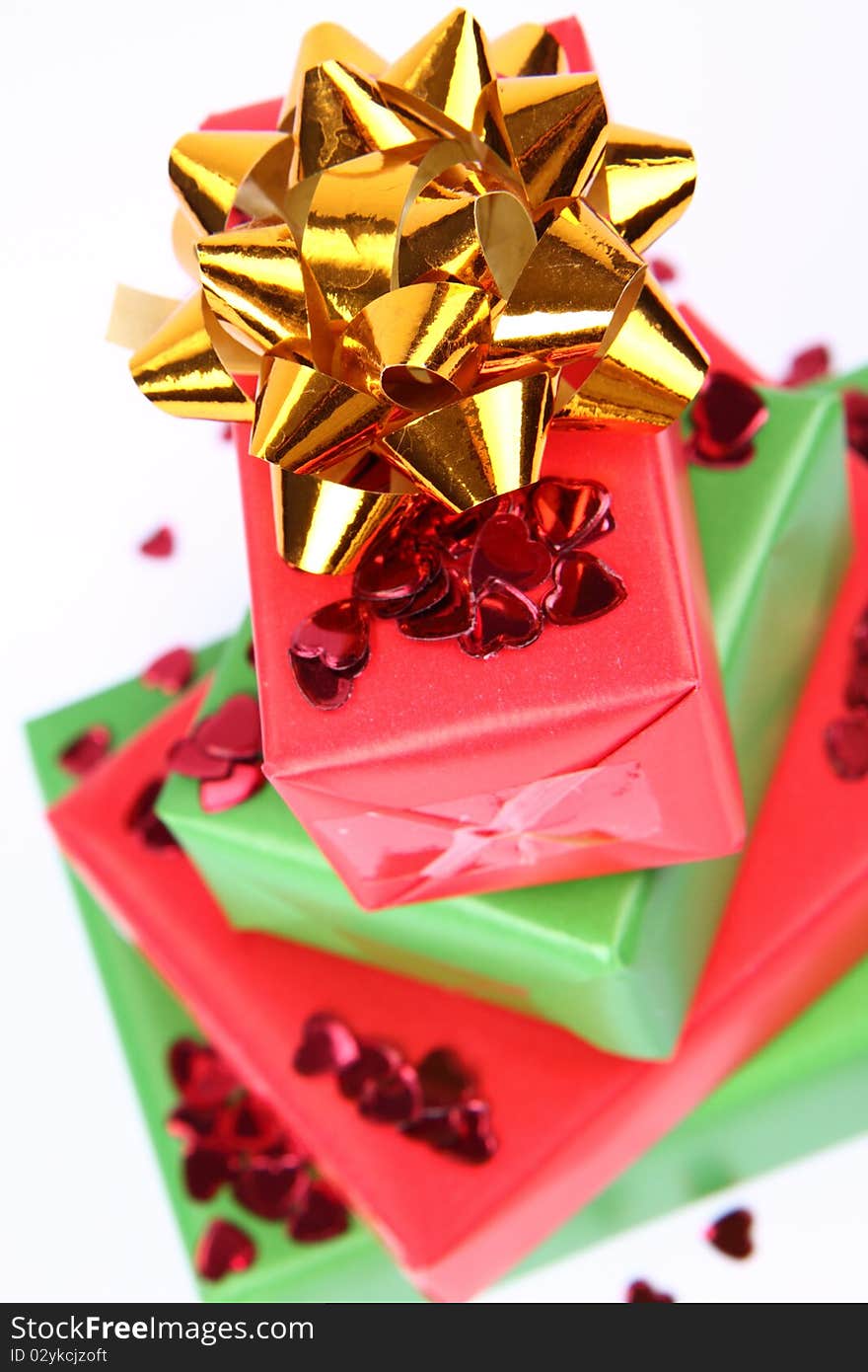 Gifts in green and red wrapping with a golden bow decorated with heart shaped confetti. Gifts in green and red wrapping with a golden bow decorated with heart shaped confetti