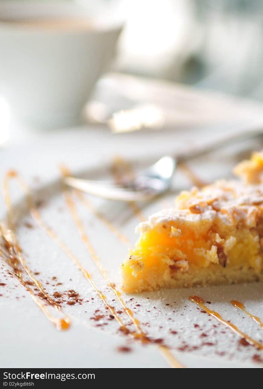 Lemon crusted top tart cake on white plate with a cup of tea in background. Lemon crusted top tart cake on white plate with a cup of tea in background.