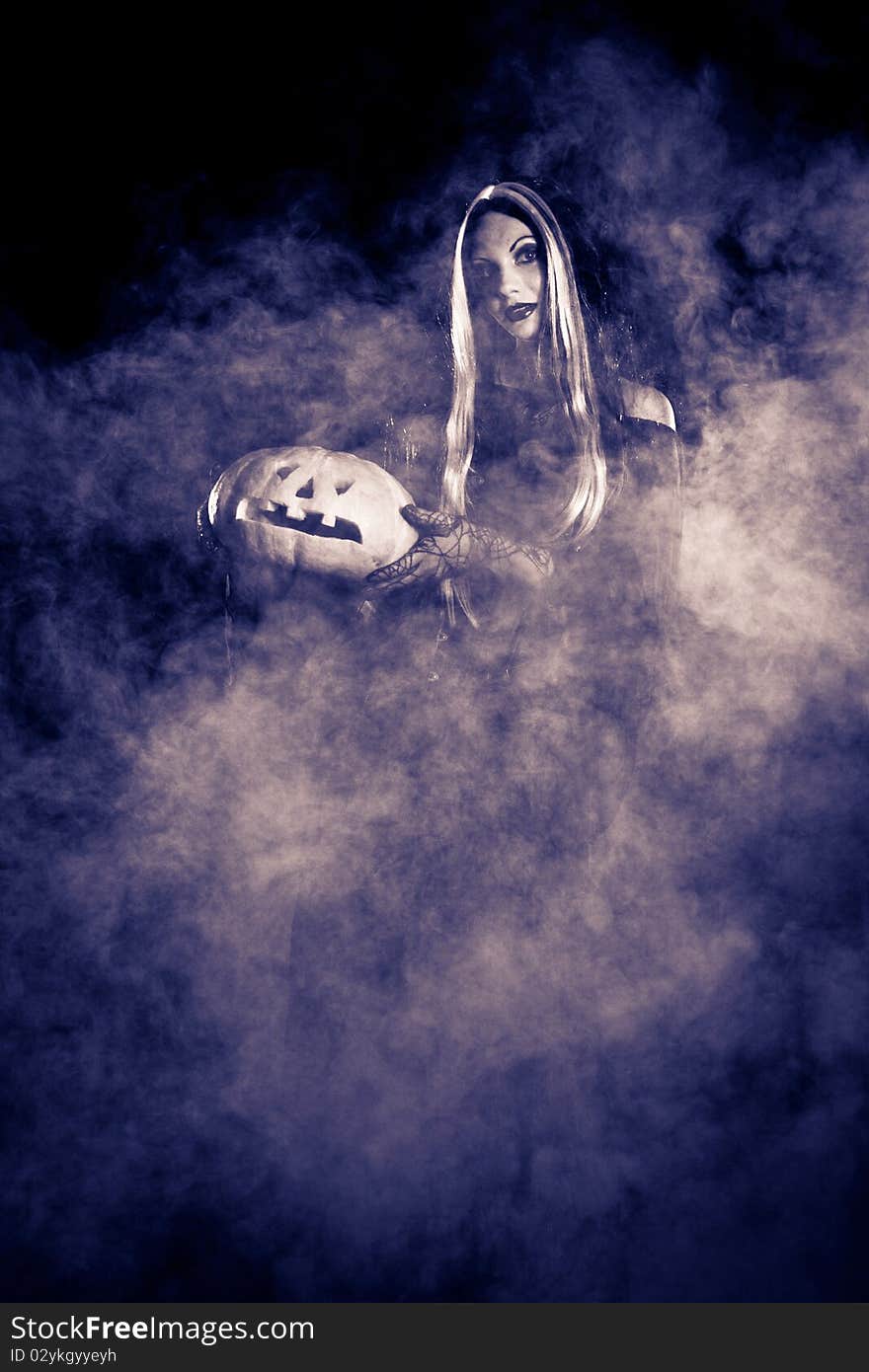 Portrait Halloween witch with a pumpkin. Smoke background