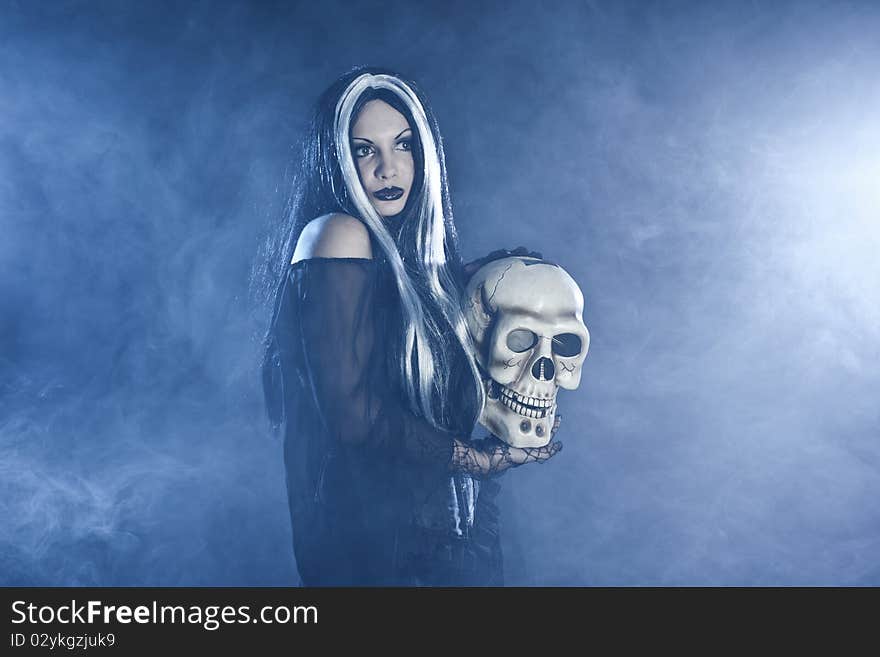 Halloween witch with a skull over black background with white smoke