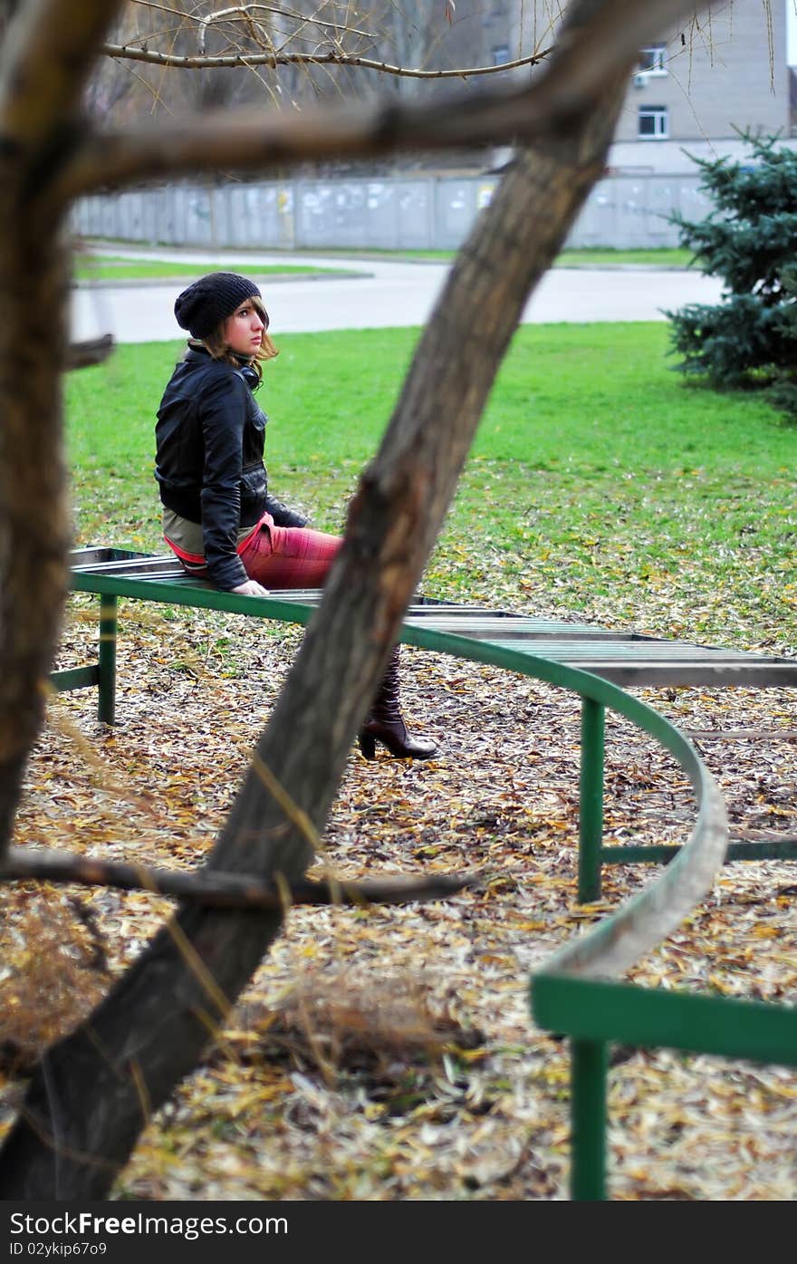 A young girl sitting on the old bench on the edge of the park. Autumn. A young girl sitting on the old bench on the edge of the park. Autumn