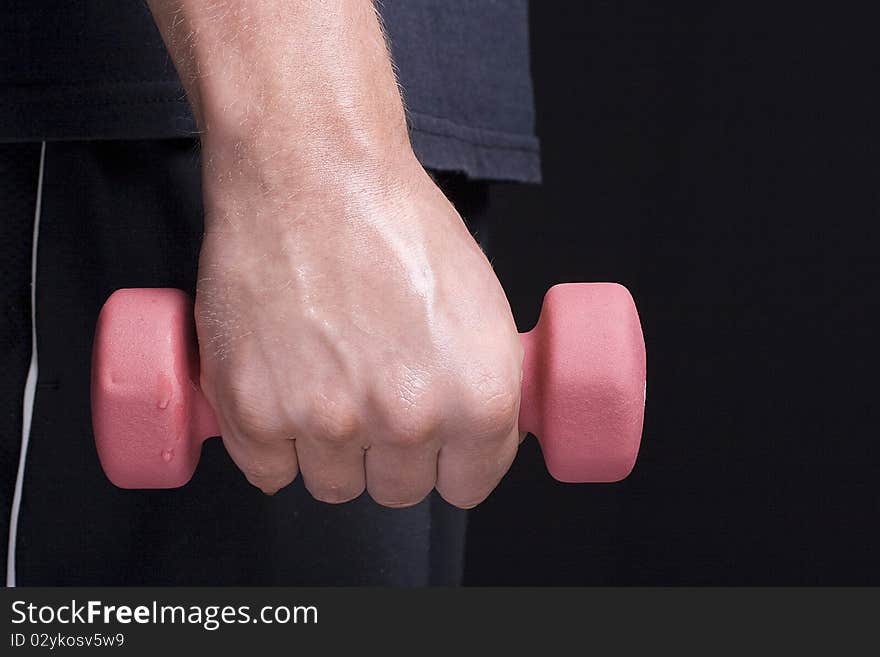 Human hand holding a pink dumbbell on a black background. Human hand holding a pink dumbbell on a black background.