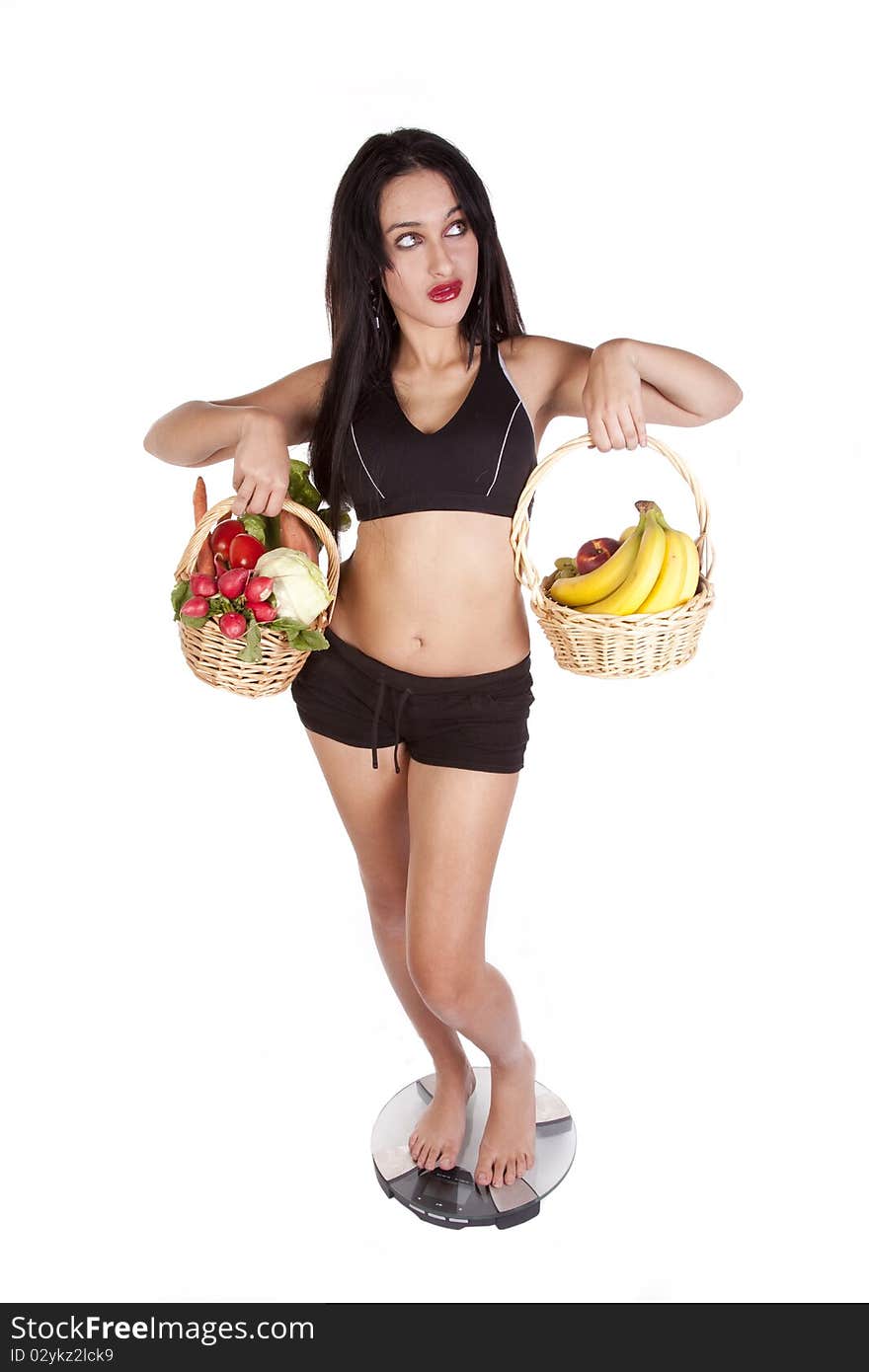 A woman is standing on the scales holding fruit and vegetables. A woman is standing on the scales holding fruit and vegetables.