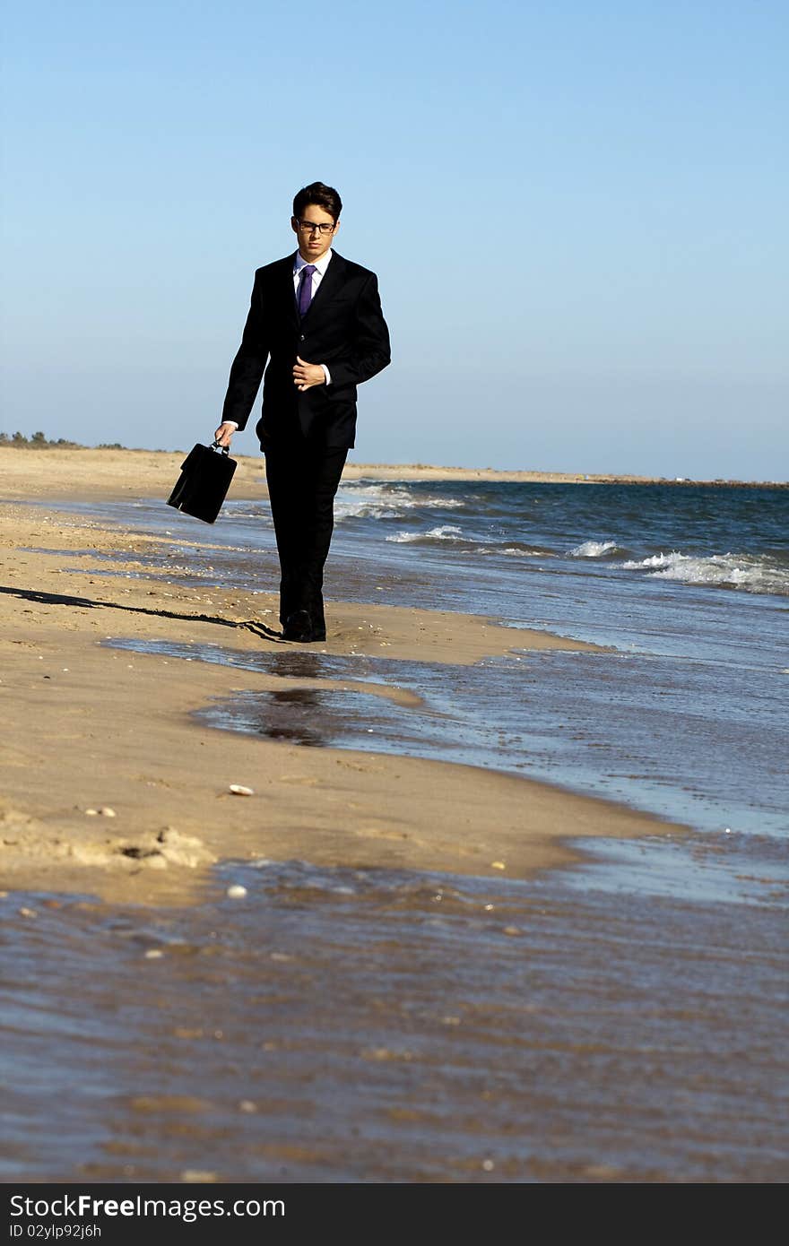 View of a young business man walking down the beach. View of a young business man walking down the beach.