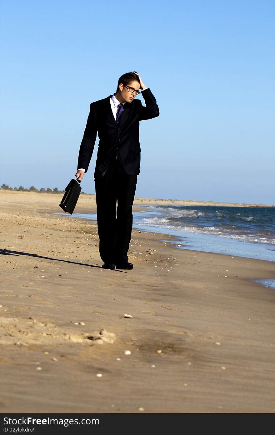 View of a young business man walking down the beach. View of a young business man walking down the beach.