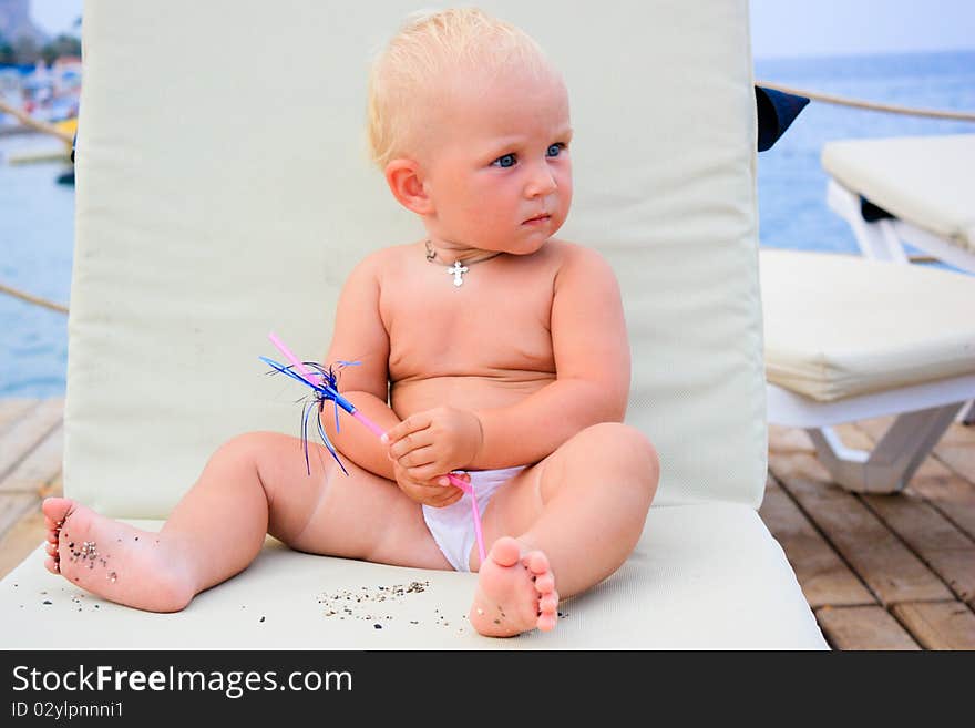 Beautiful baby's sitting with cocktail straw on a beach chair on a pier. Beautiful baby's sitting with cocktail straw on a beach chair on a pier