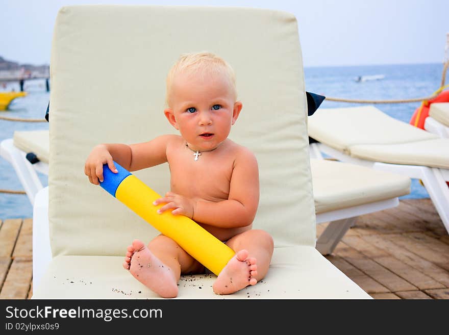 Beautiful baby's sitting with water toy on a beach chair on a pier. Beautiful baby's sitting with water toy on a beach chair on a pier