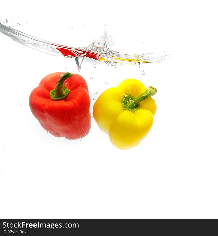 Red and yellow peppers splashing into water over white