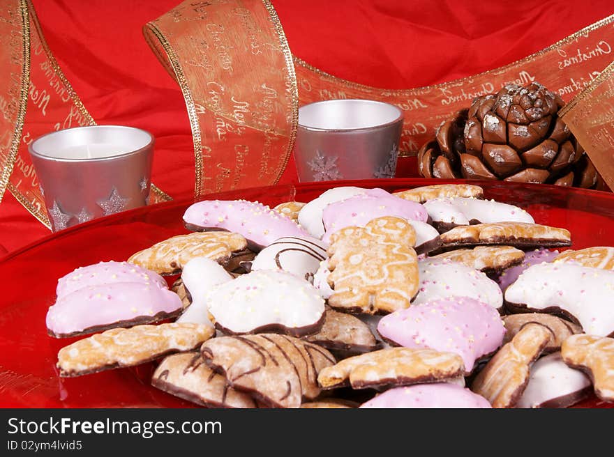 Gingerbread cookies in a red plate with silver candles, pine cones and Christmas ribbon. Studio shot over red background. Shallow DOF. Gingerbread cookies in a red plate with silver candles, pine cones and Christmas ribbon. Studio shot over red background. Shallow DOF.