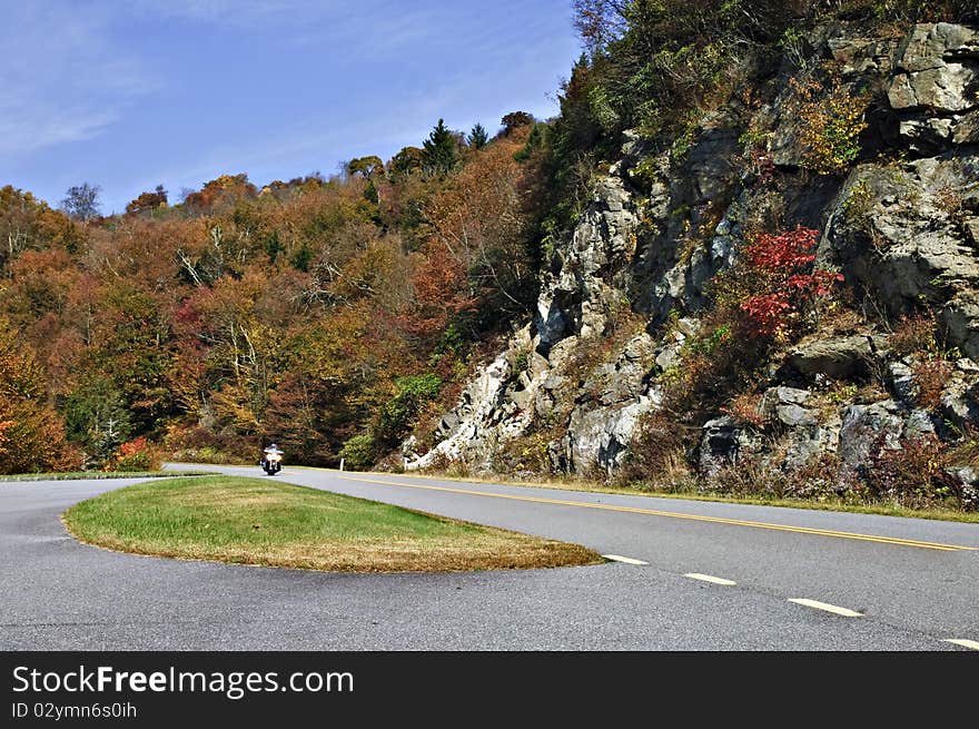 Motorcyclist coming around the curve on a highway in autumn. Motorcyclist coming around the curve on a highway in autumn.