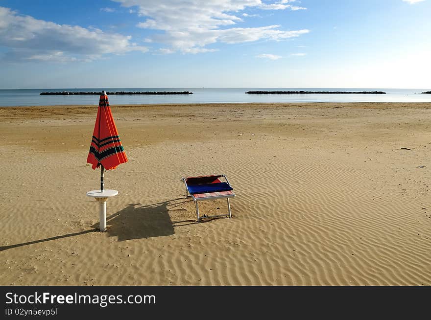 Orange umbrella and sunbed on a deserted beach in early morning