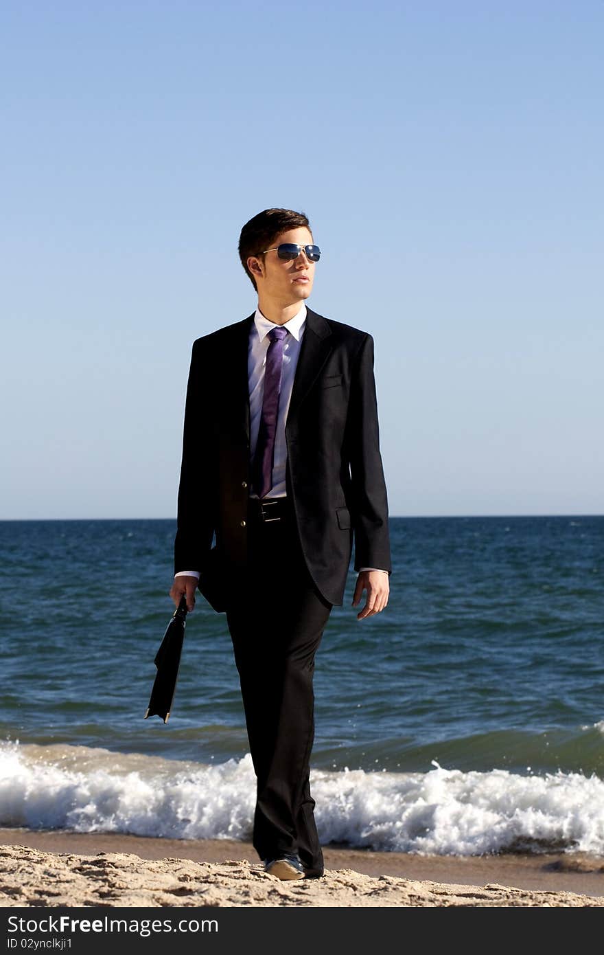 View of a young business man walking down the beach. View of a young business man walking down the beach.