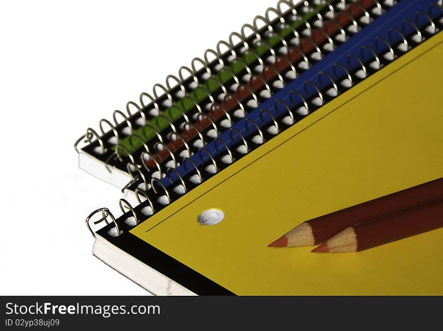 Blue, red, yellow and green school notebooks with red pencils on white background. Soft focus on pencil points. Copy space. Blue, red, yellow and green school notebooks with red pencils on white background. Soft focus on pencil points. Copy space.