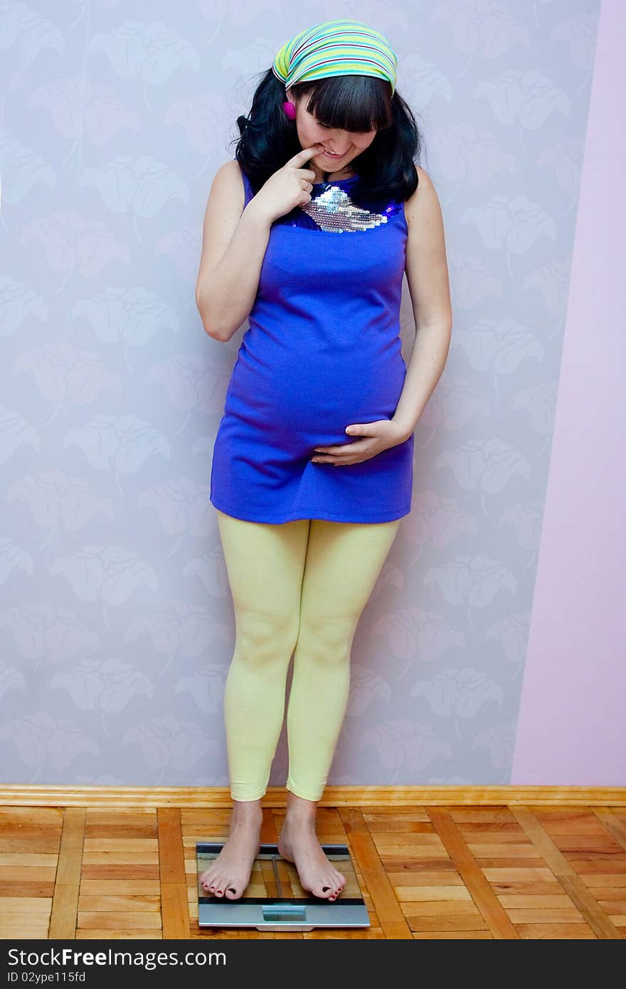 Pregnant woman standing on scales and holding her baby bump