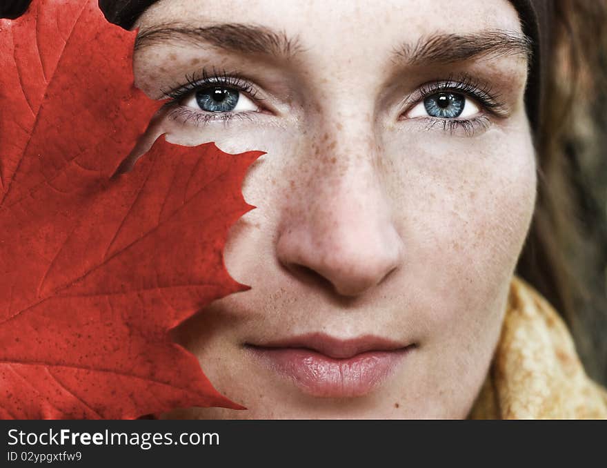 Woman face-half hidden behind the red leaf. Woman face-half hidden behind the red leaf