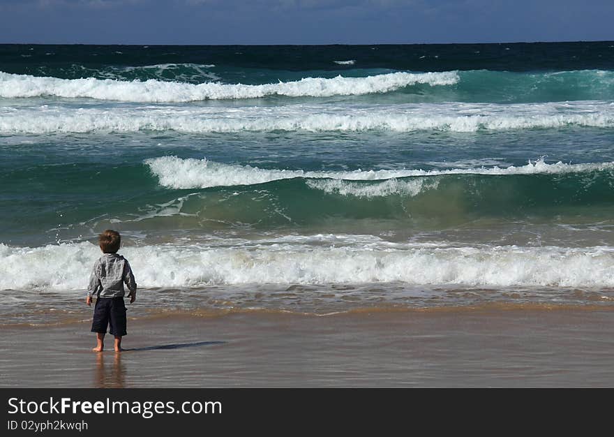 3-year-old boy looks at the sea. Autumn sea, strong waves, sharp colors.