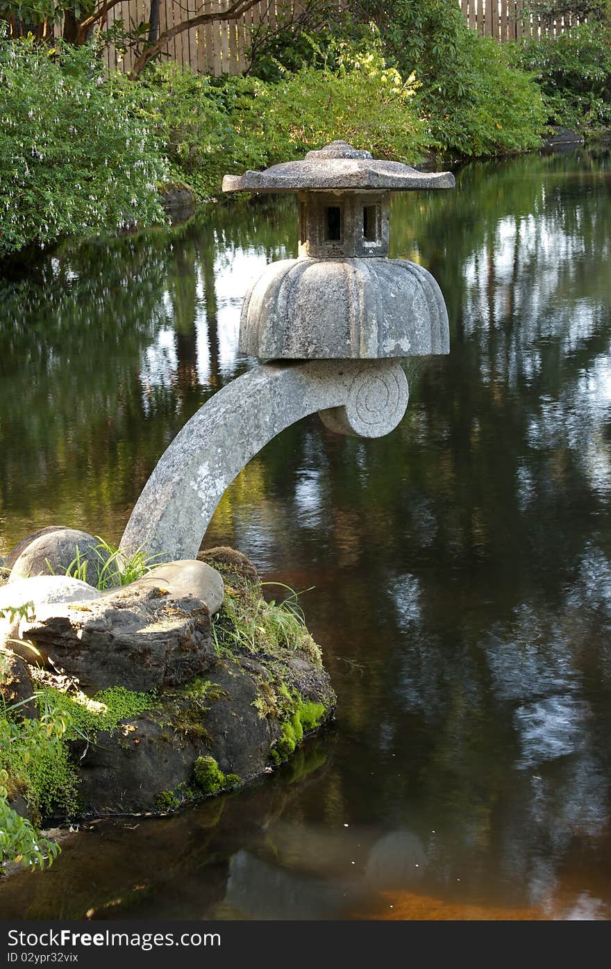 A zen cement lantern decoration above a garden pond. A zen cement lantern decoration above a garden pond.