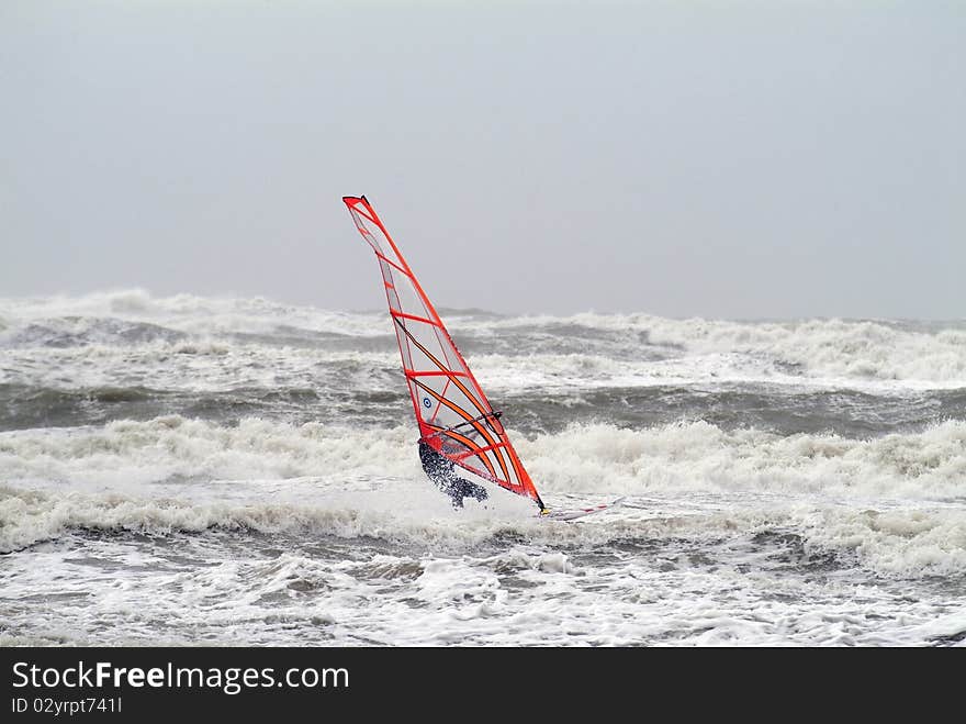 Surfer on windsurf with red sail on stormy sea with big wawes. Surfer on windsurf with red sail on stormy sea with big wawes