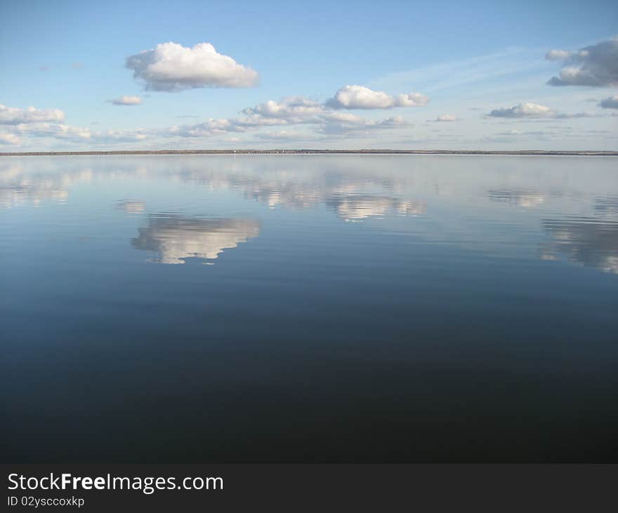 Cumulus white clouds over big quiet lake. Clouds are reflected in water. Cumulus white clouds over big quiet lake. Clouds are reflected in water.