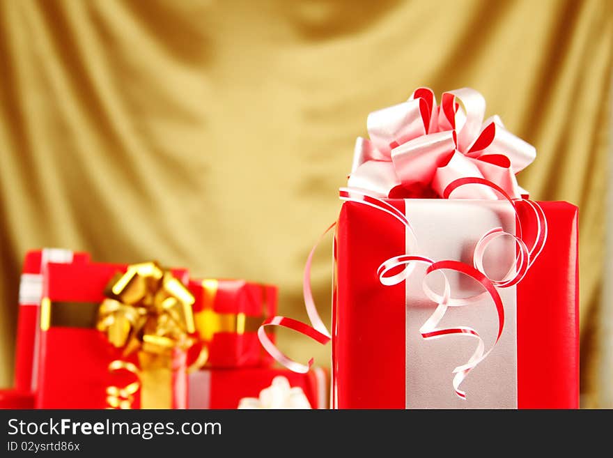 A lot of Christmas presents different values in the red packages with colorful bows on a gold background. A lot of Christmas presents different values in the red packages with colorful bows on a gold background