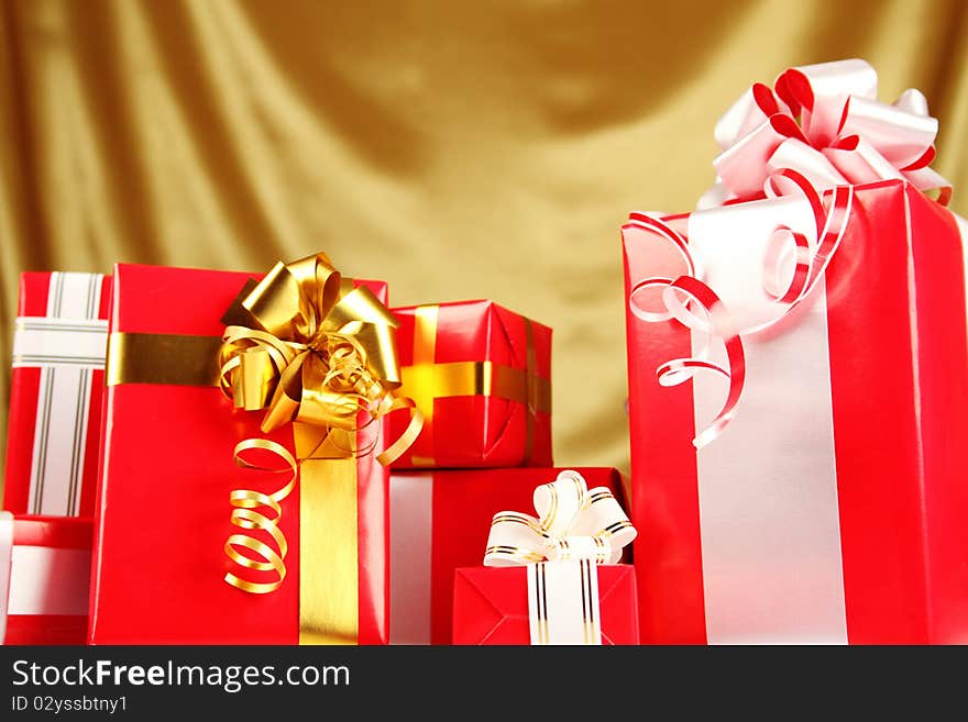 A lot of Christmas presents different values in the red packages with colorful bows on a gold background. A lot of Christmas presents different values in the red packages with colorful bows on a gold background