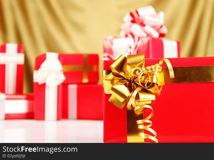 A lot of Christmas presents different values in the red packages with colorful bows on a gold background. A lot of Christmas presents different values in the red packages with colorful bows on a gold background