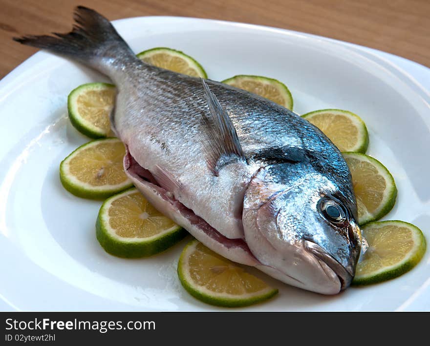 Fresh gilthead fish with slices of lemon on the plate, waiting to be cooked