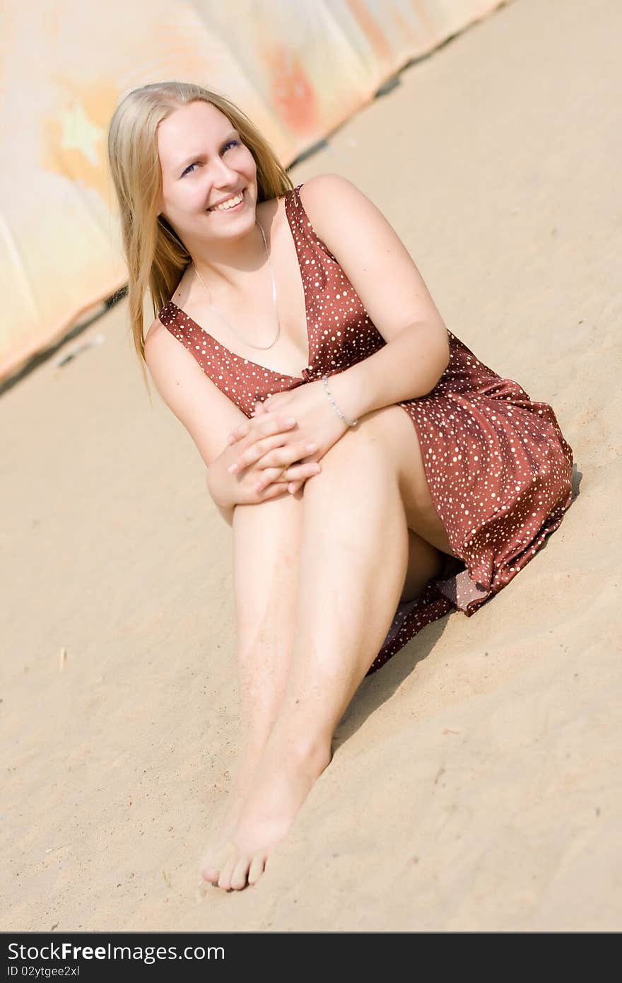 Summer portrait of the beautiful fair-haired girl who seat on the sand