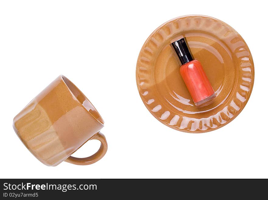 Orange nail polish laying on a brown plate next to a brown cup.