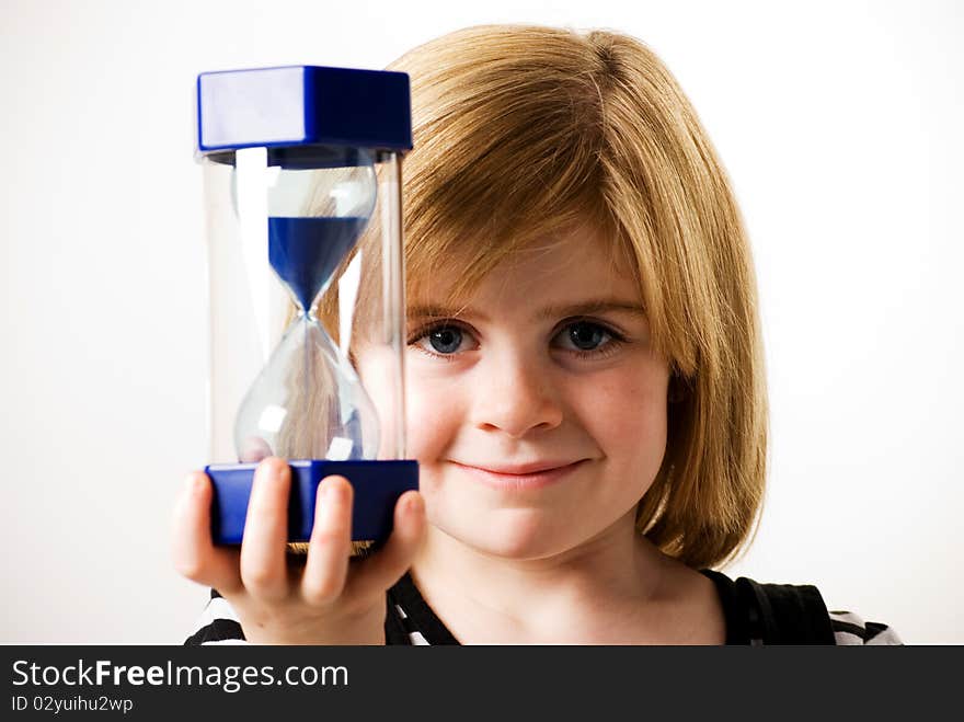 A vertical image of a young girl looking at the sand flowing in a hourglass. A vertical image of a young girl looking at the sand flowing in a hourglass