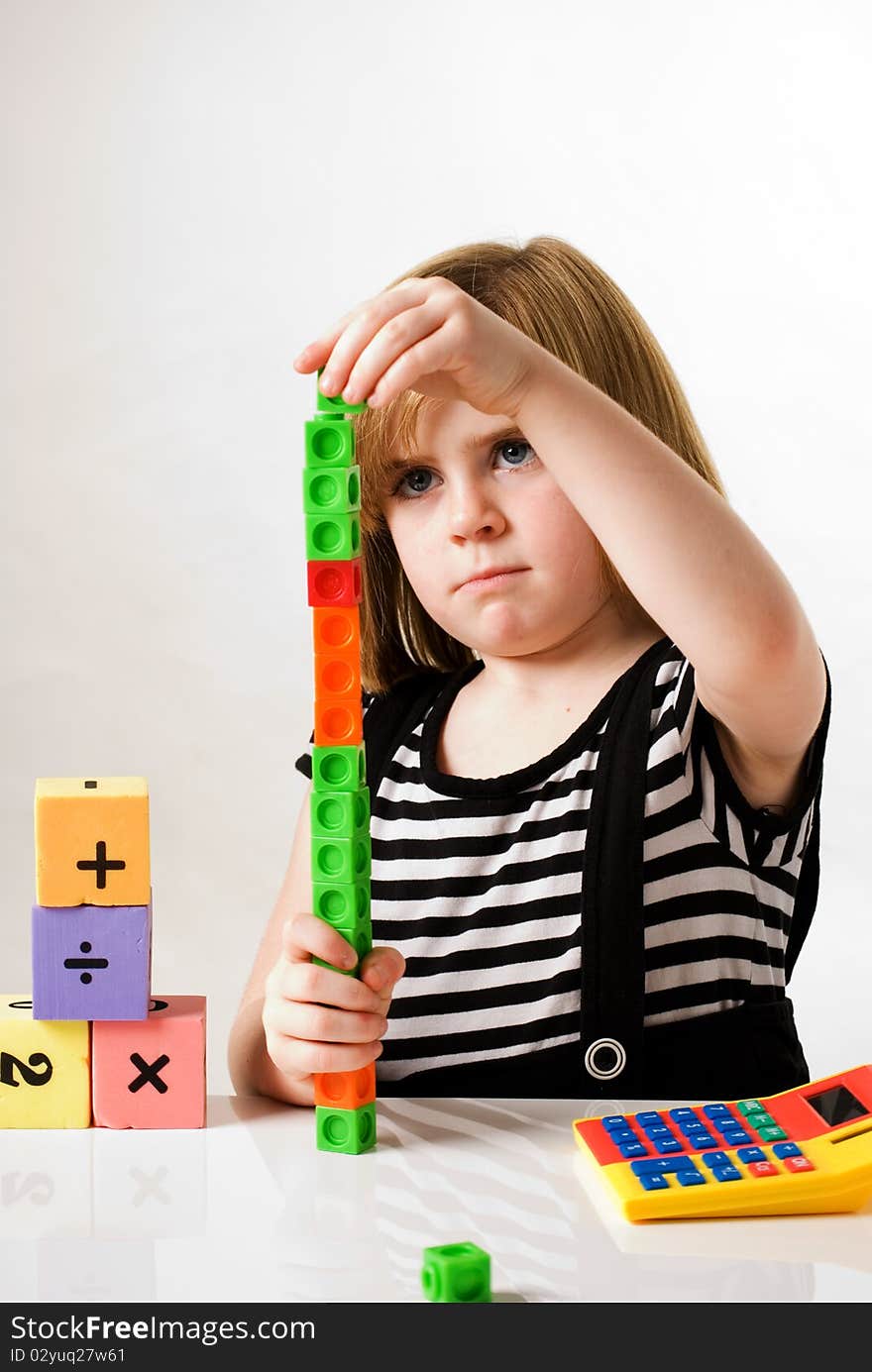 A vertical image of a young girl with counting blocks , building blocks and calculator.