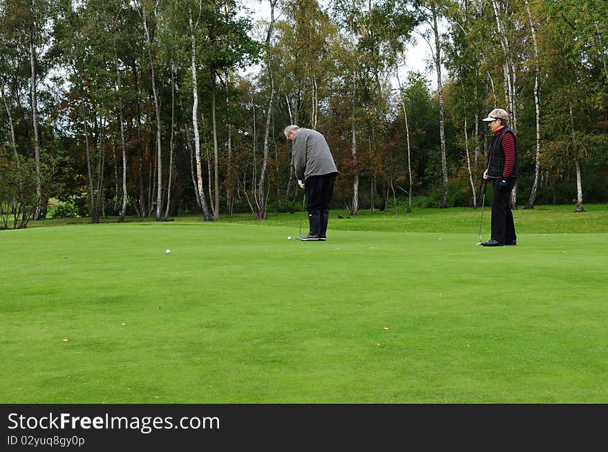 Male golfer preparing to put on the green while a female golfer is watching. Male golfer preparing to put on the green while a female golfer is watching