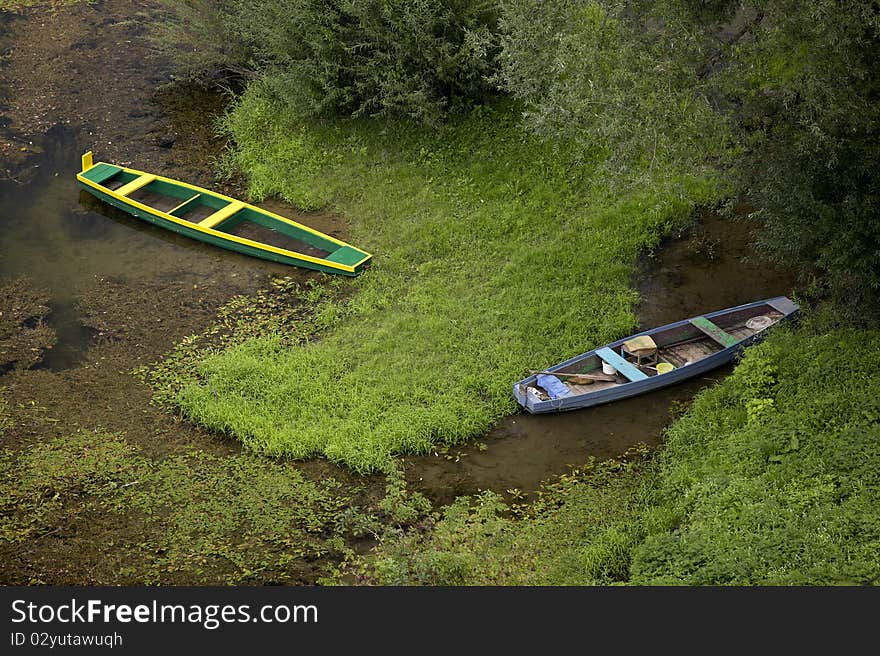 2 wooden river boats, shallow river, green grass and trees