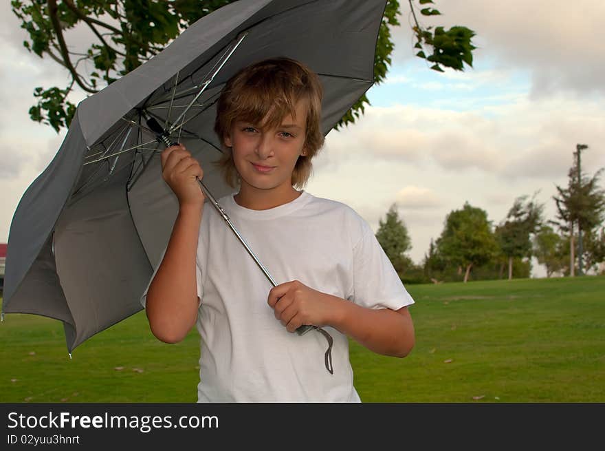 Boy looking at camera while under umbrella outside  . Boy looking at camera while under umbrella outside  .