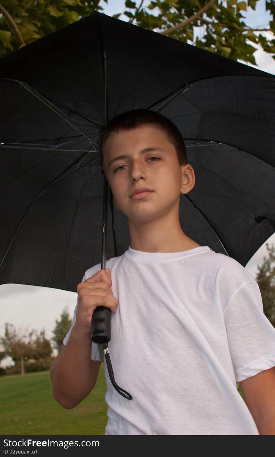 Boy looking at camera while under umbrella outside  . Boy looking at camera while under umbrella outside  .