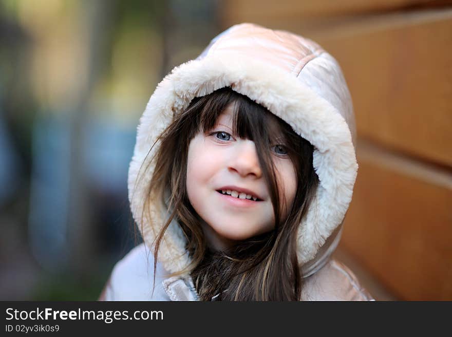 Adorable small girl with long dark hair in colorful warm clothes looks into the camera