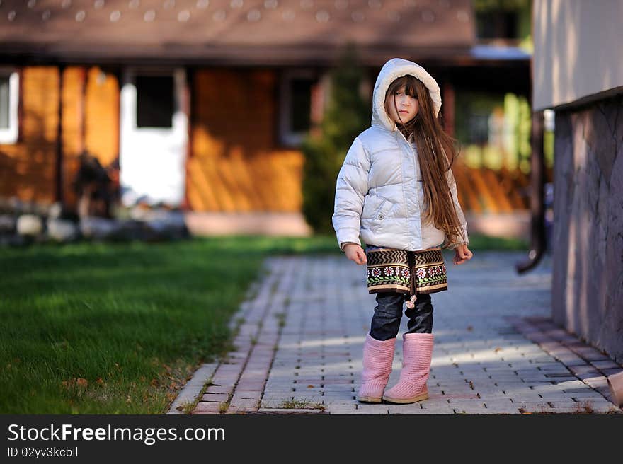 Adorable small girl with long dark hair in colorful warm clothes looks into the camera