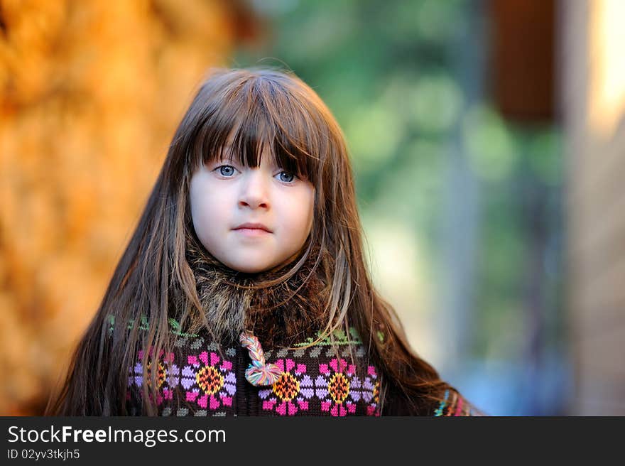 Adorable small girl with long dark hair in colorful warm clothes looks into the camera