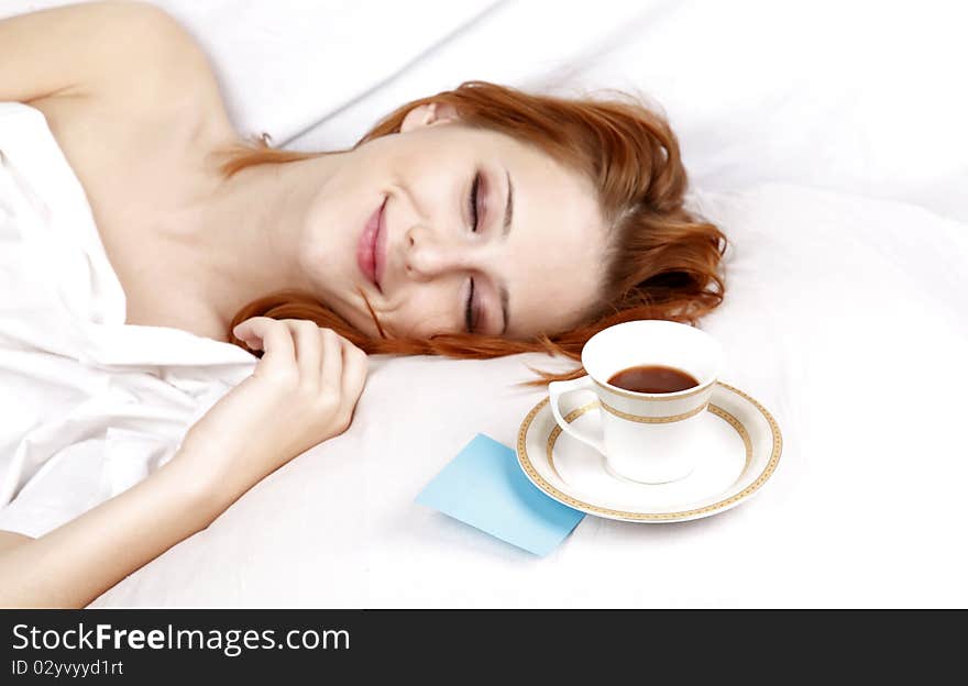 Pretty red-haired sleeping woman in white nightie lying in the bed near cup of coffee. Pretty red-haired sleeping woman in white nightie lying in the bed near cup of coffee.