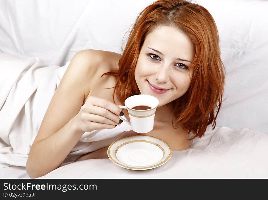 Pretty red-haired woman in white nightie lying in the bed near cup of coffee. Pretty red-haired woman in white nightie lying in the bed near cup of coffee.