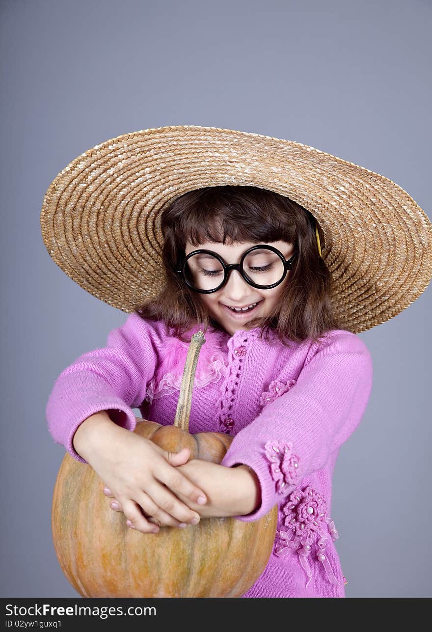 Funny girl in cap and glasses keeping pumpkin. Studio shot.