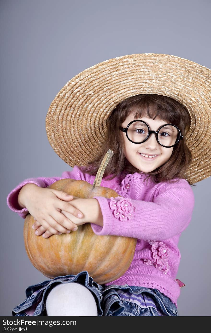 Funny girl in cap and glasses keeping pumpkin.