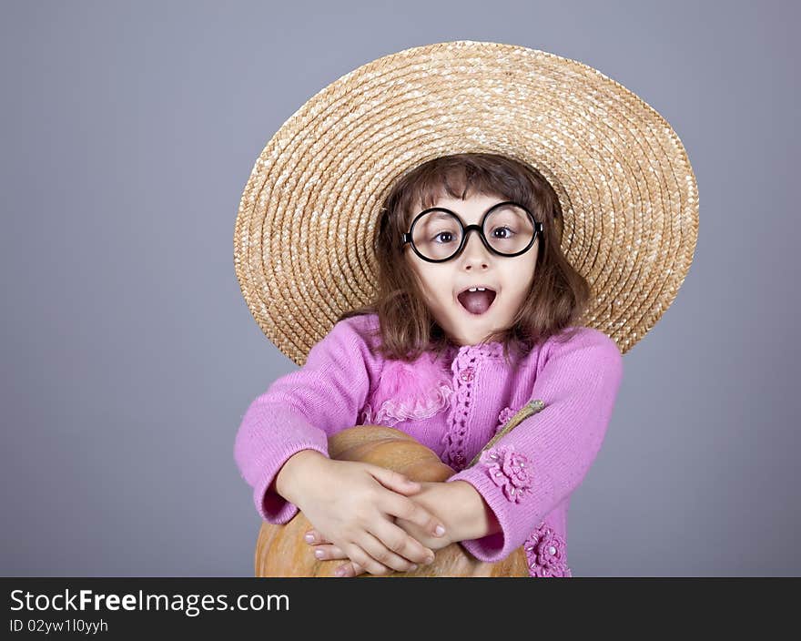 Funny girl in cap and glasses keeping pumpkin. Studio shot.