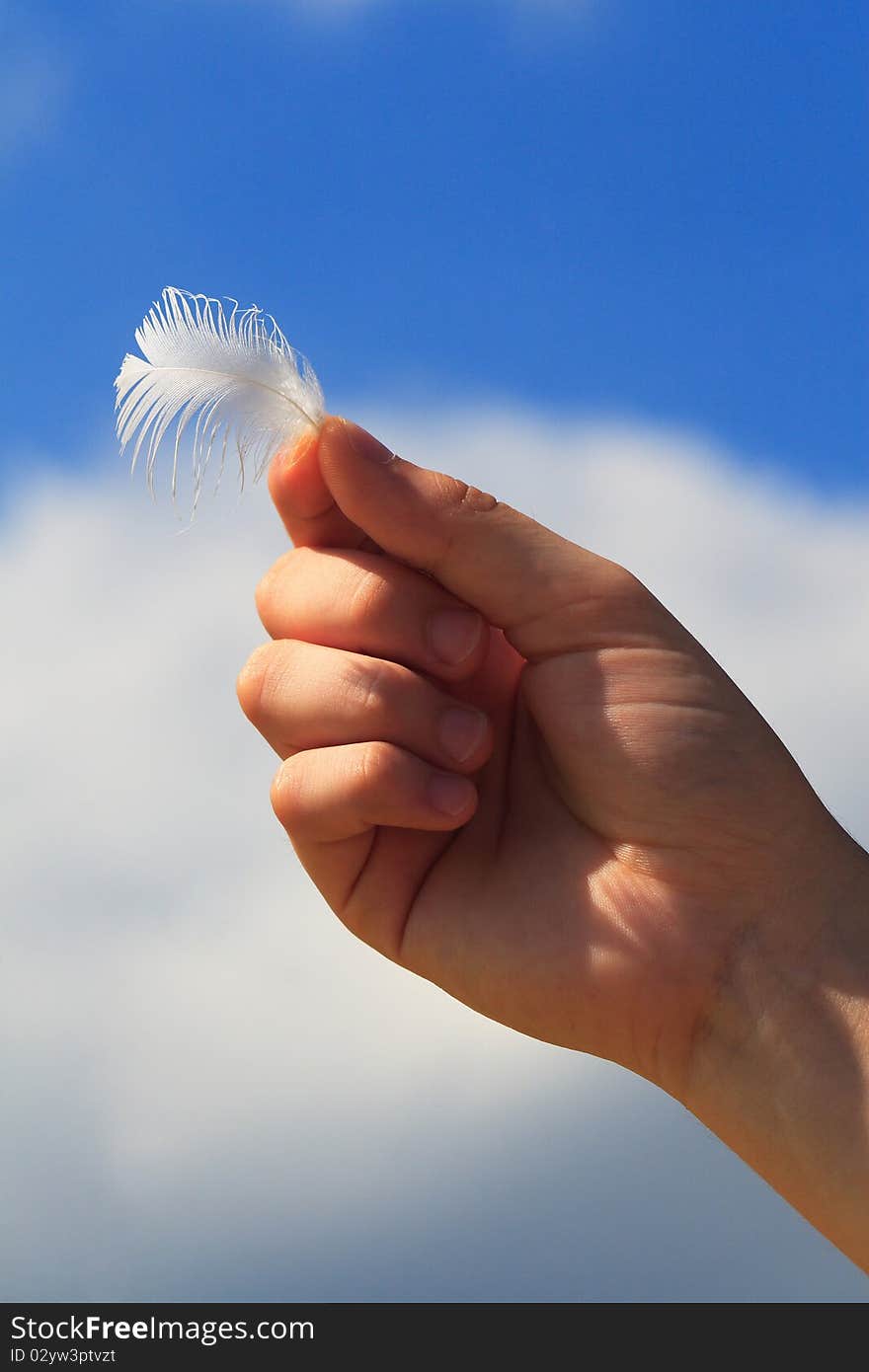 Hand holds a feather against blue sky