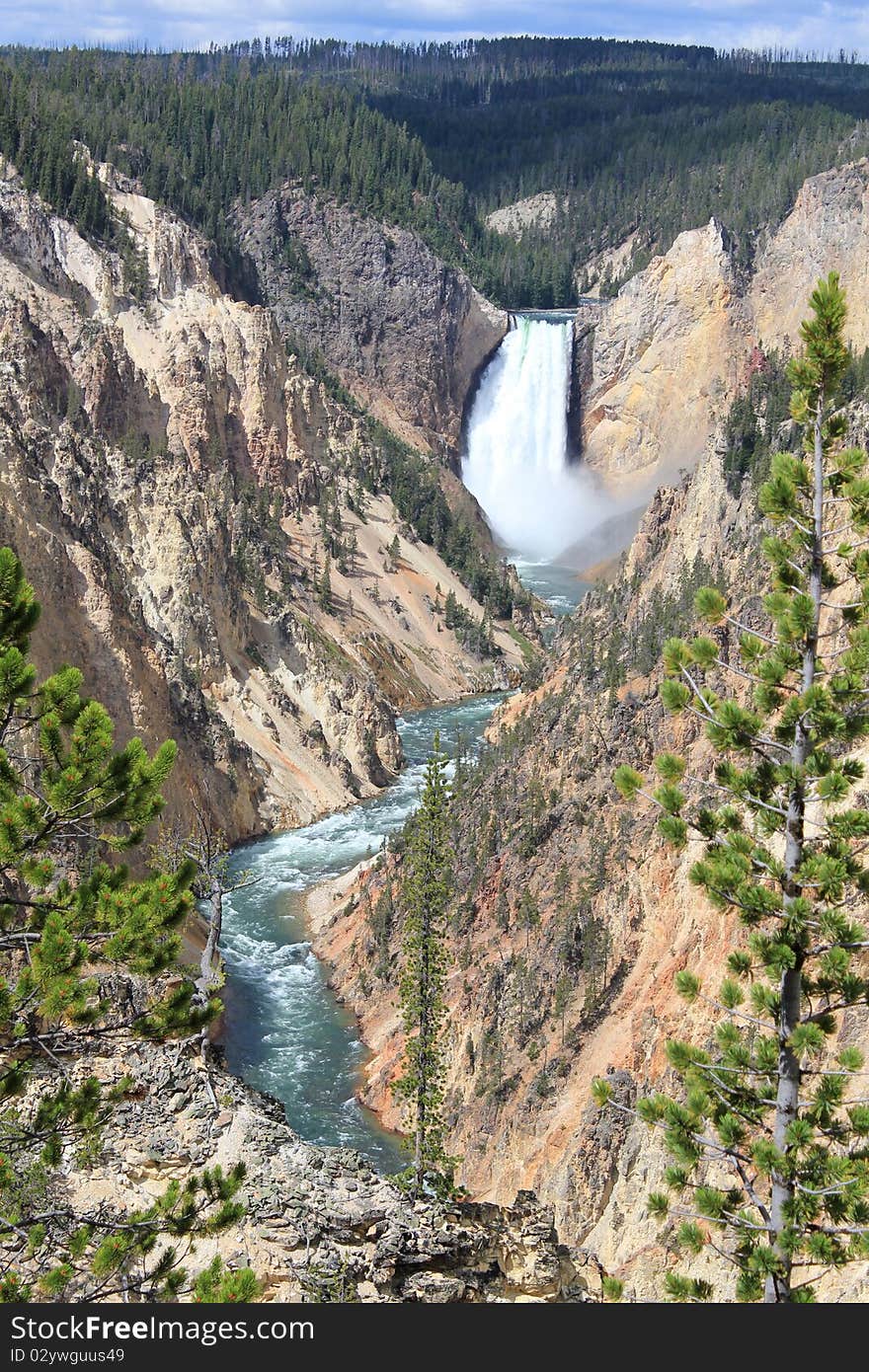 Large waterfall flows into a river below between large mountains with trees. Large waterfall flows into a river below between large mountains with trees