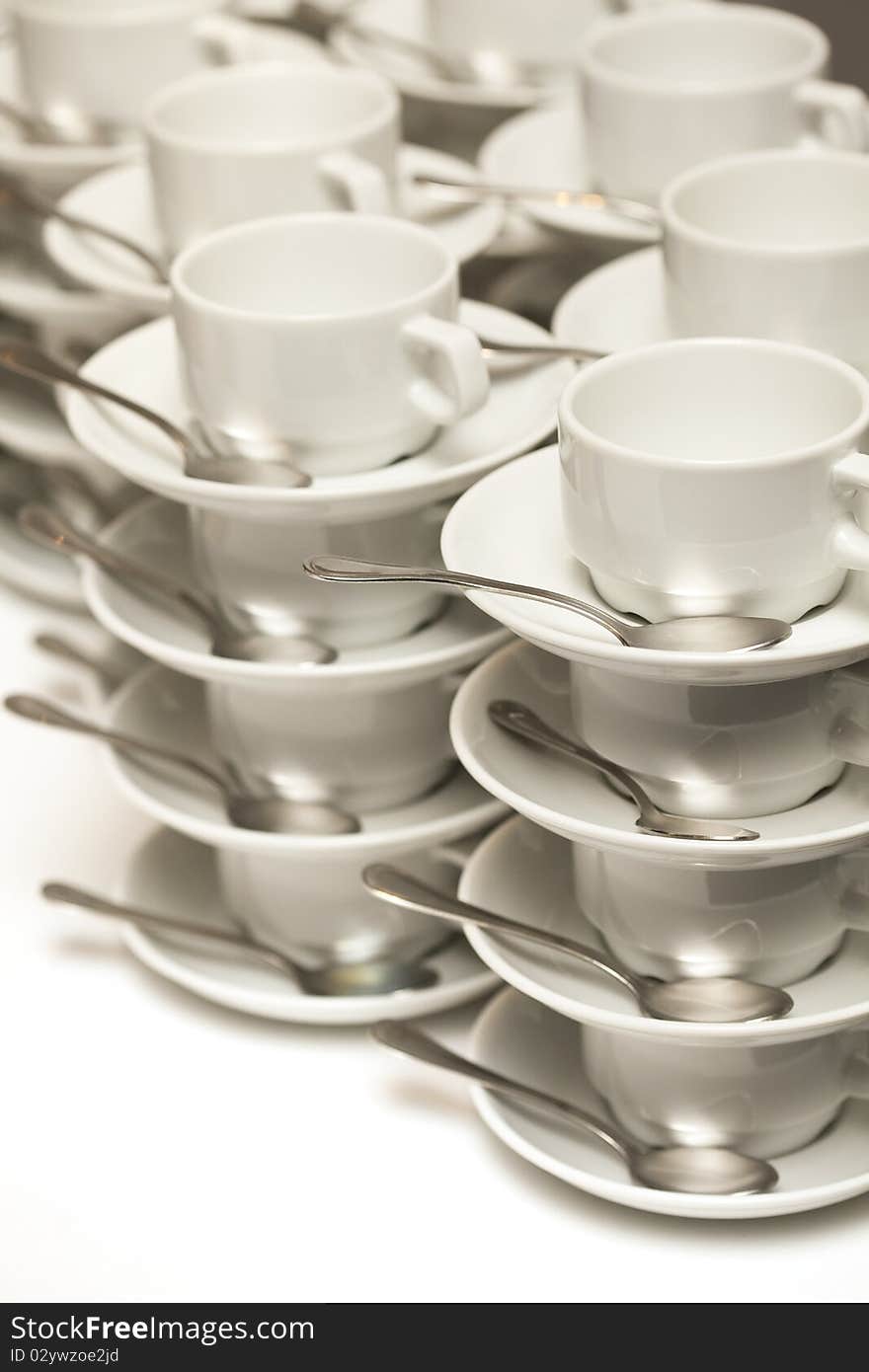 Stacked empty teacups with teaspoons at a function over white background